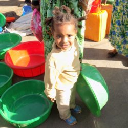 This photo shows a small girl holding a large green plastic washing-up bowl
