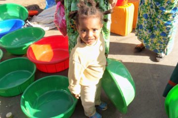 This photo shows a small girl holding a large green plastic washing-up bowl