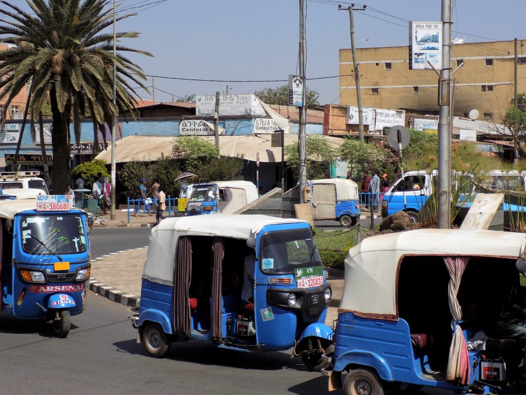 This photo shows several blue and white bajajs negotiating a roundabout in the centre of Bahir Dar