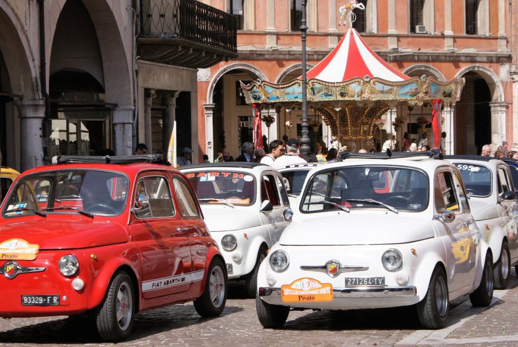 This photo shows funky red and white Fiat 500s with a colourful carousel in the background
