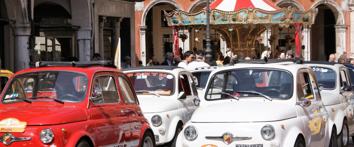 This photo shows funky red and white Fiat 500s with a colourful carousel in the background