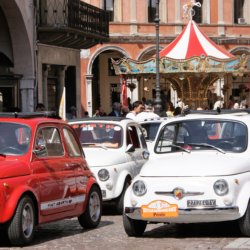 This photo shows funky red and white Fiat 500s with a colourful carousel in the background