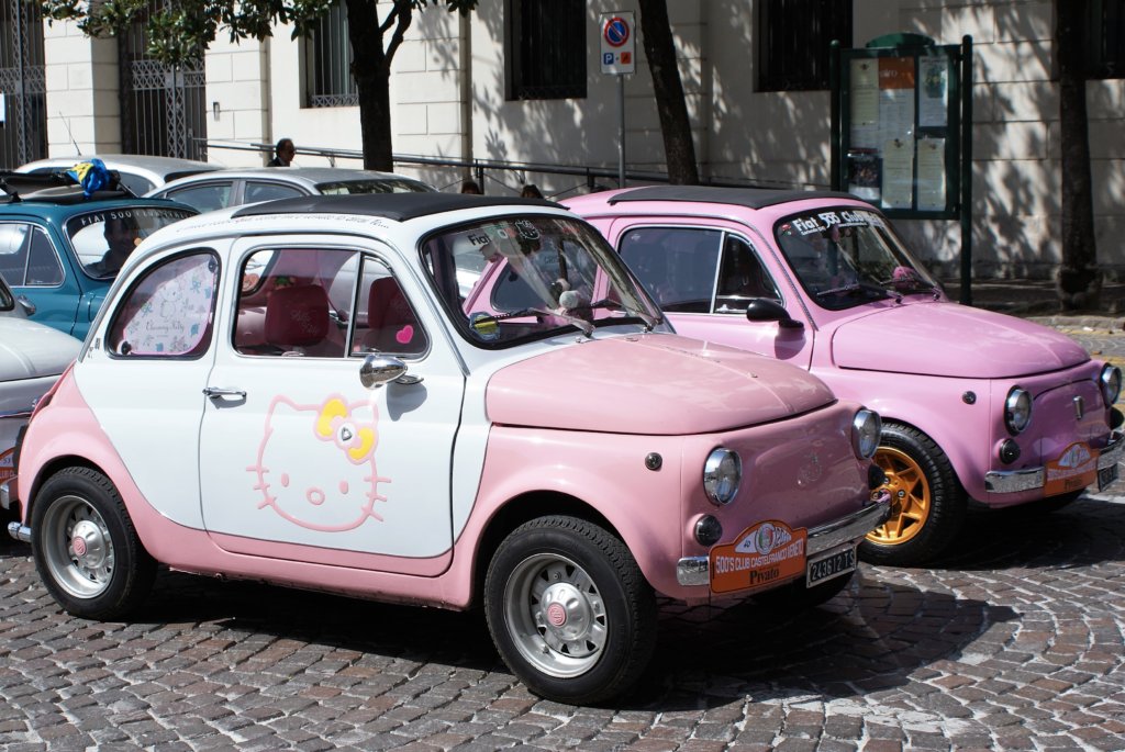 This photo shows two baby-pink Fiat 500s one of which is decorated with Hello Kitty images