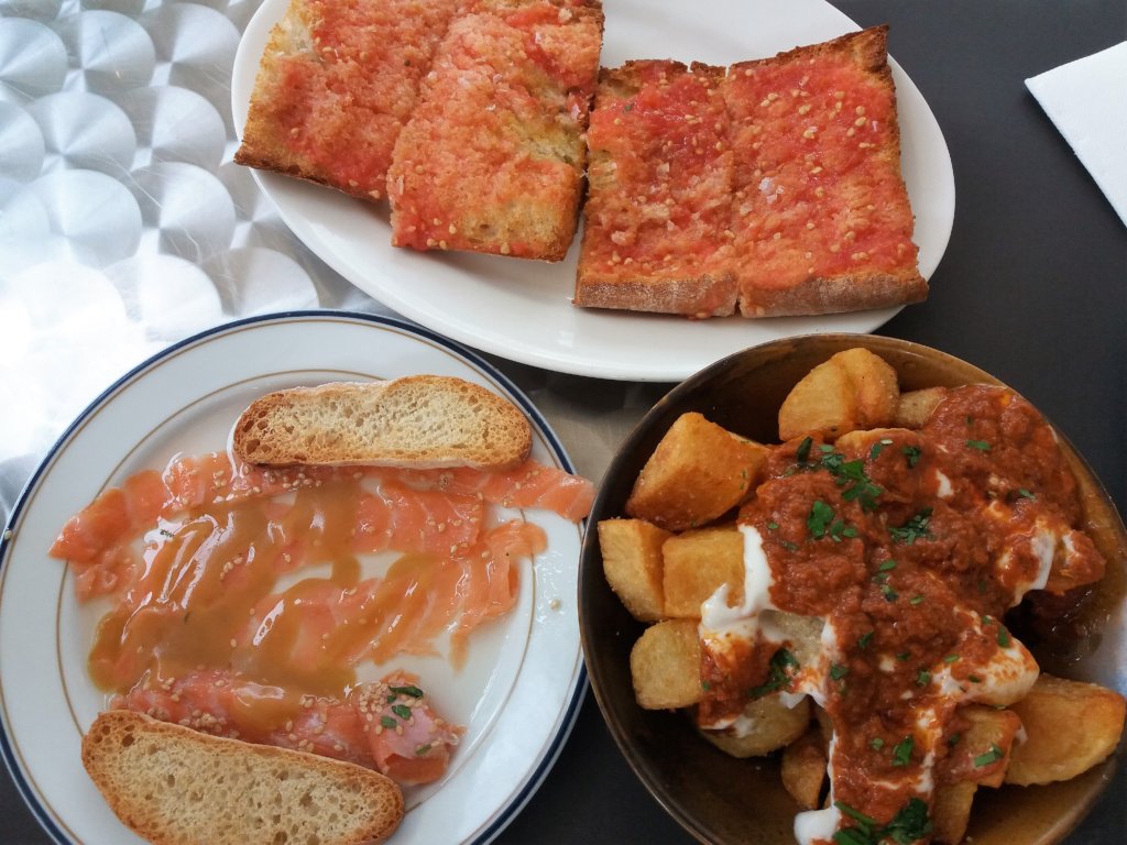 This photo shows tomato bread, marinated salmon and patatas bravas