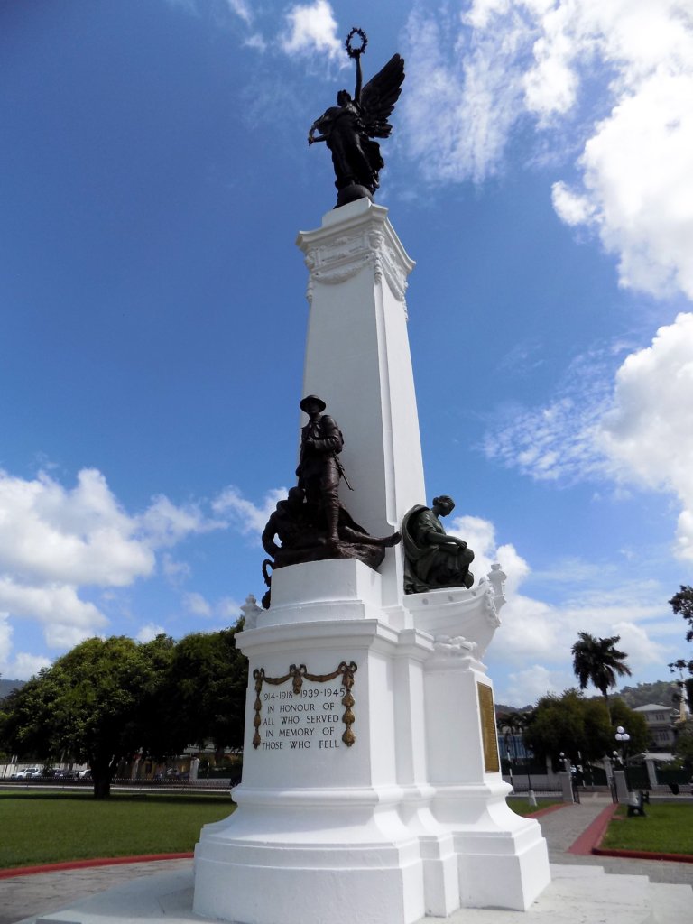 This photo shows a crisp white memorial adorned with black statues and gold lettering set against a brilliant blue sky