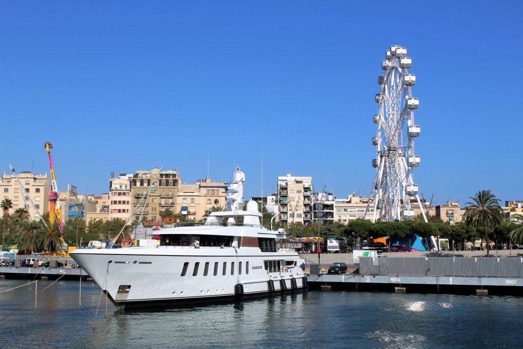 This photo shows a gleaming white pleasure boat moored in front of Barcelona's big wheel