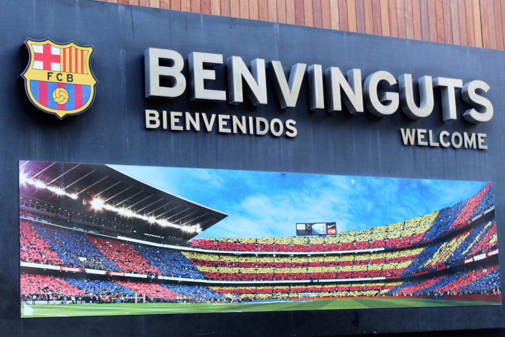 This photo shows the welcome sign at Camp Nou with a picture of a full stadium