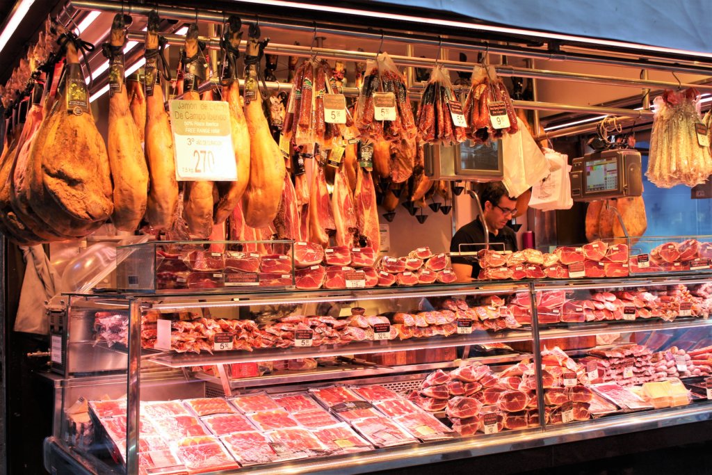 This photo shows a ham stall with whole legs of jamon hanging up behind the main display of cured pork
