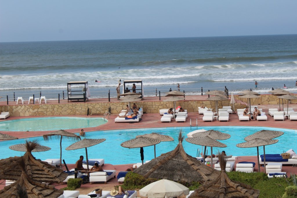 This photo shows a beach club with swimming pool, loungers and palm tree sunshades