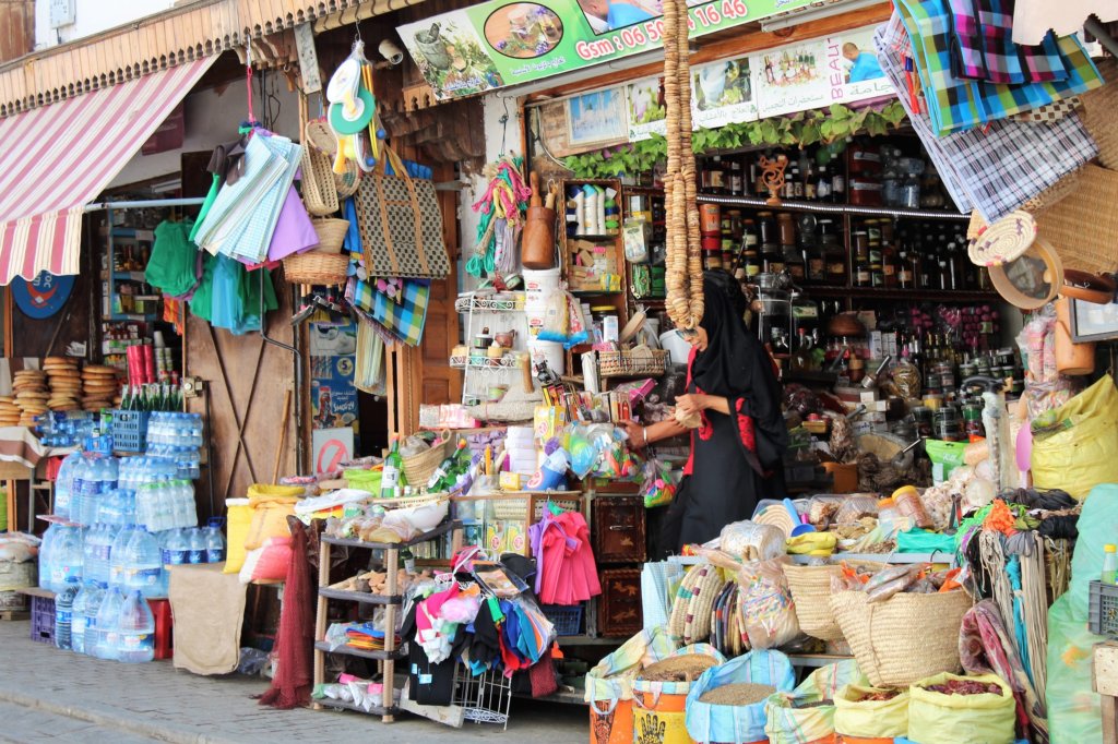 This photo shows a stall packed with colourful household goods including brooms, buckets and shopping bags