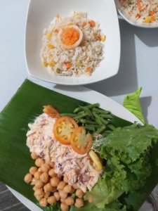 This photo shows green beans, coleslaw, lettuce and chick peas served on a banana leaf with a side dish of vegetable rice