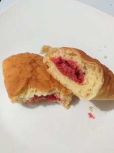 This photo shows a coconut tart broken in two to show the red-coloured filling