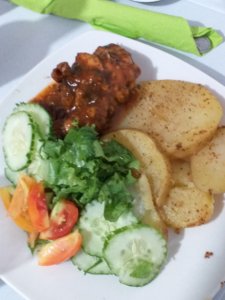 This photo shows a plate of sticky barbecue chicken, sliced potatoes and salad