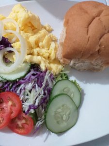 This photo shows a plate of scrambled egg and salads with a wholemeal roll