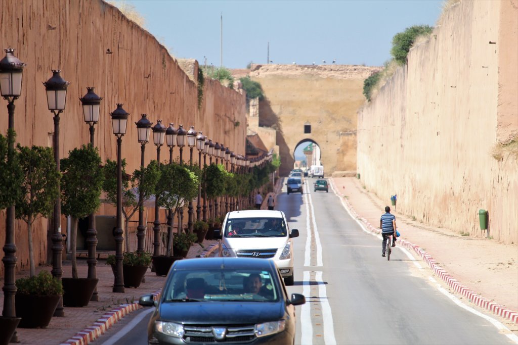 This photo shows a road with cars with thick fortified walls on either side and straight ahead