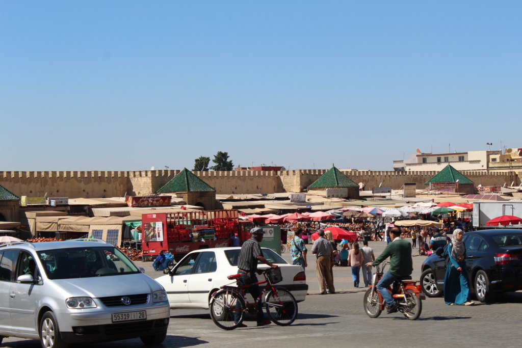 This picture shows the busy square crowded with stalls, pedestrians, cars and cyclists