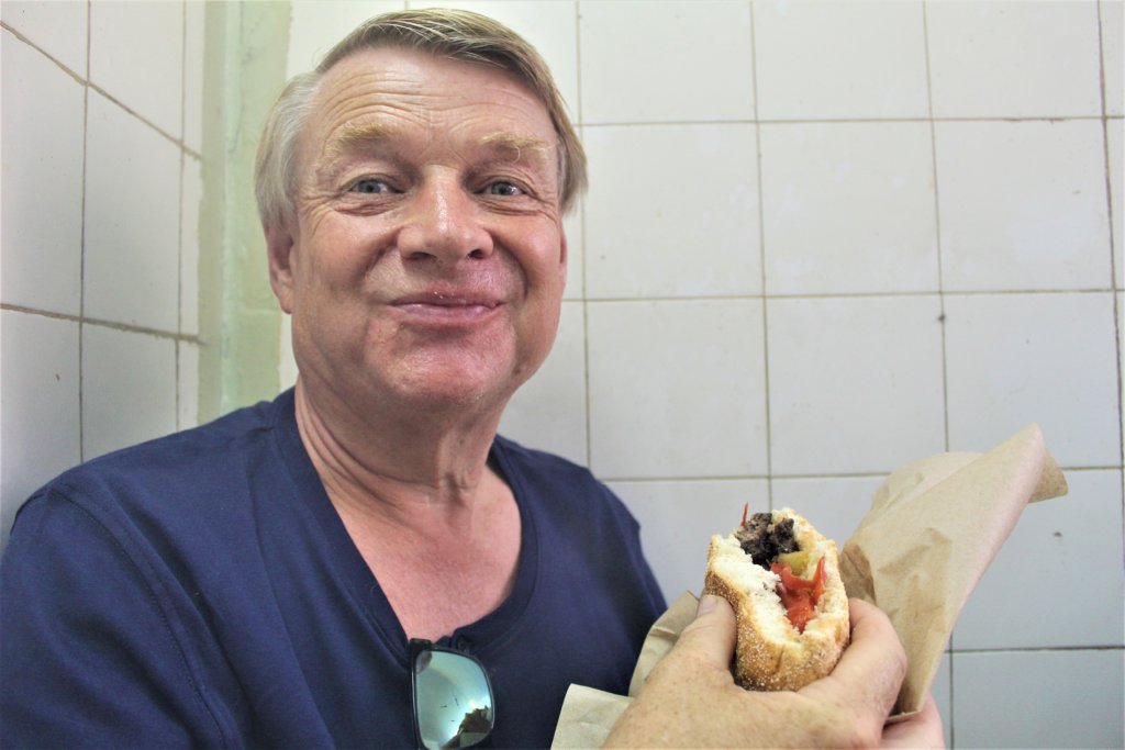 This photo shows Mark smiling at the camera and holding a camel burger