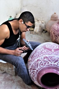 This photo shows a man hammering a pattern into a large ceramic planter