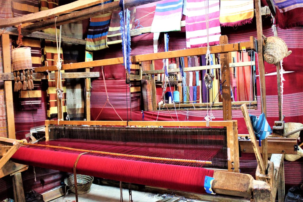 This photo shows some red woollen fabric being woven on ahand loom