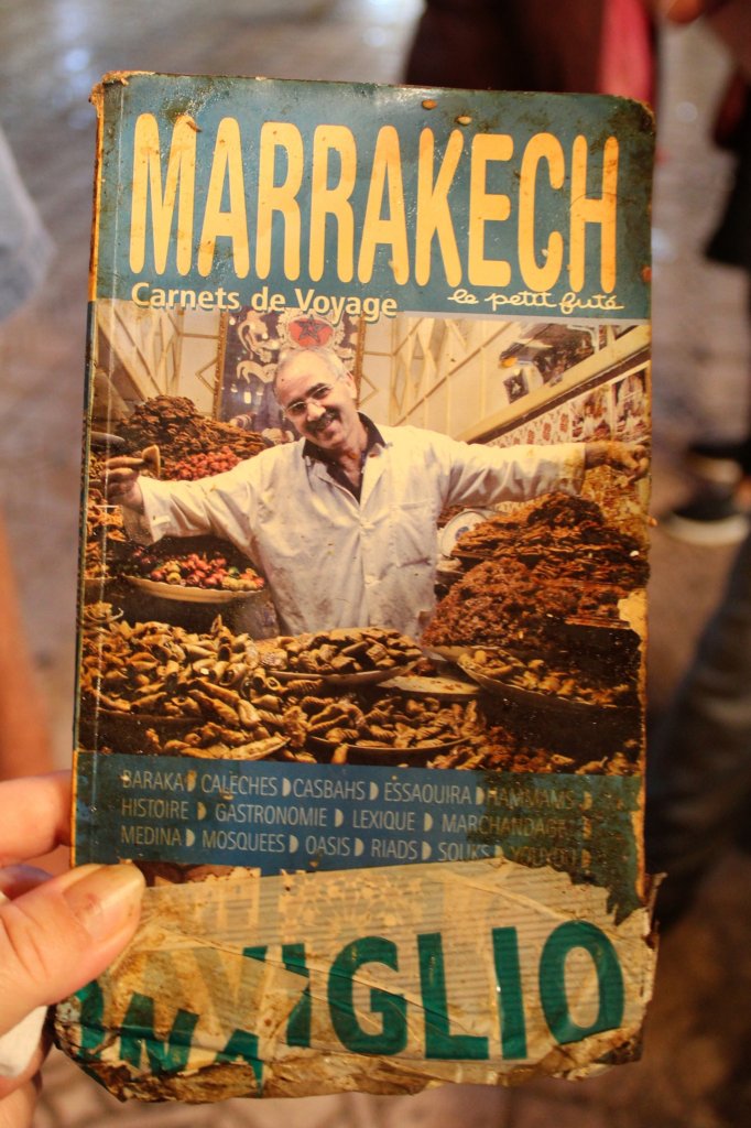 This photo shows an old guide book of Marrakech with a picture of the cookie seller on the cover