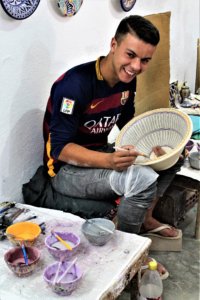 This photo shows a smiling painter decorating a finished tagine lid