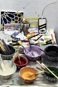 This photo shows pots of different coloured paints and numerous paint brushes