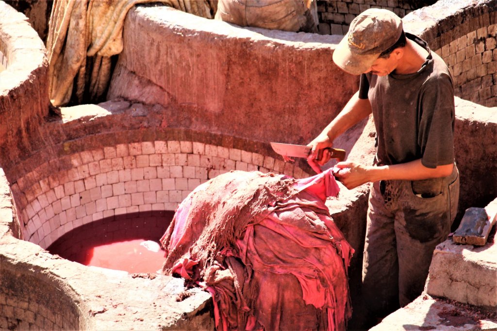 This photo shows a man scraping a hide that is being dyed red