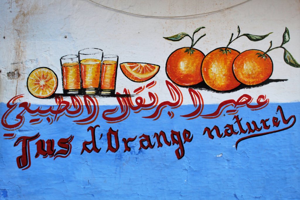 This photo shows hand painted oranges and glasses of orange juice on a blue and white painted wall