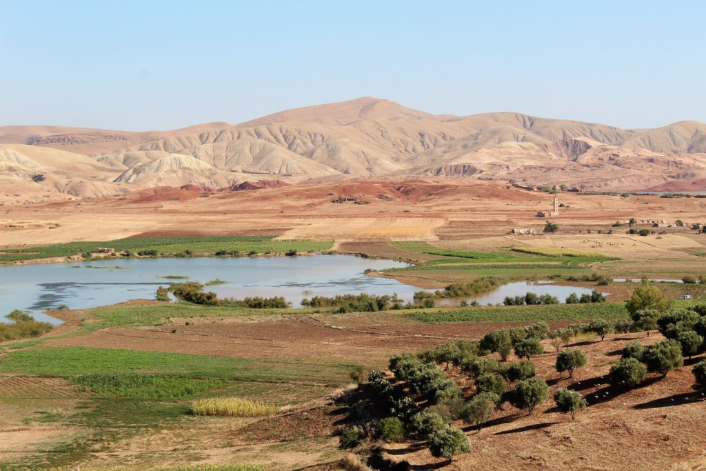 This photo shows a lake with mountains behind and fields in the foreground