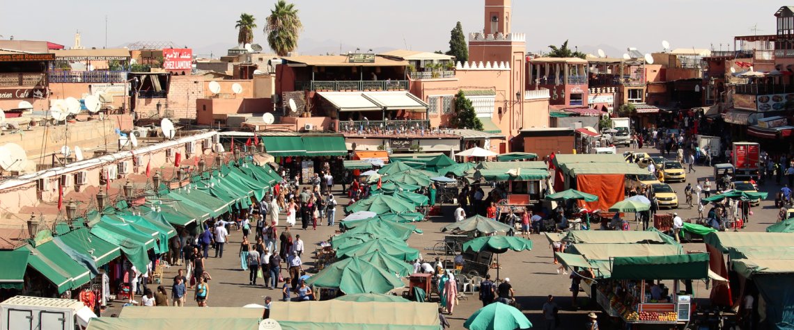 This photo shows Djemaa el-Fna with lots of stalls topped with green tarpaulins or umbrellas