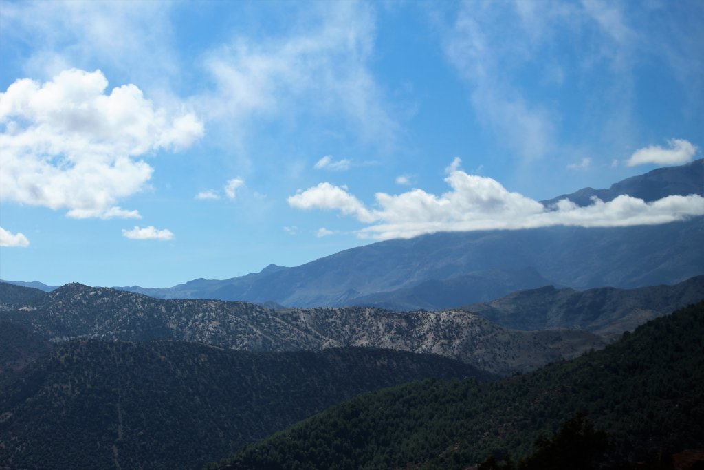 This photo shows white fluffy clouds passing in front of a mountain in an otherwise clear blue sky