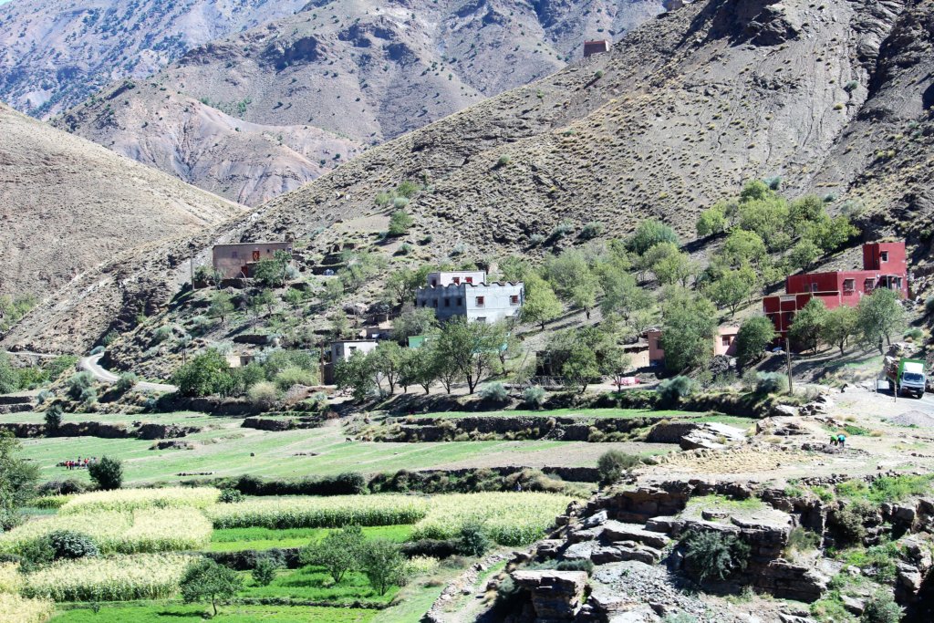 This photo shows a small village nestled at the base of a mountain with green fields in the foreground