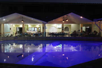 This photo shows the pool at night illuminated from underneath so that the water looks purple and you can see the restaurant reflected in it.