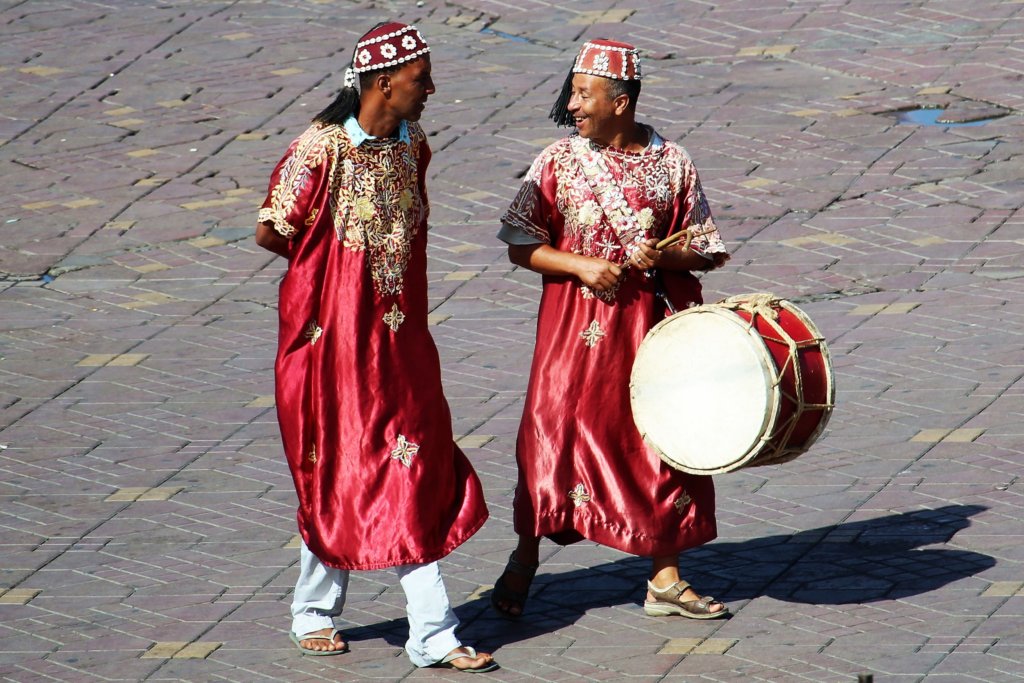 This photo shows two musicians walking across Djemaa el-Fna. One of them is carrying a drum.