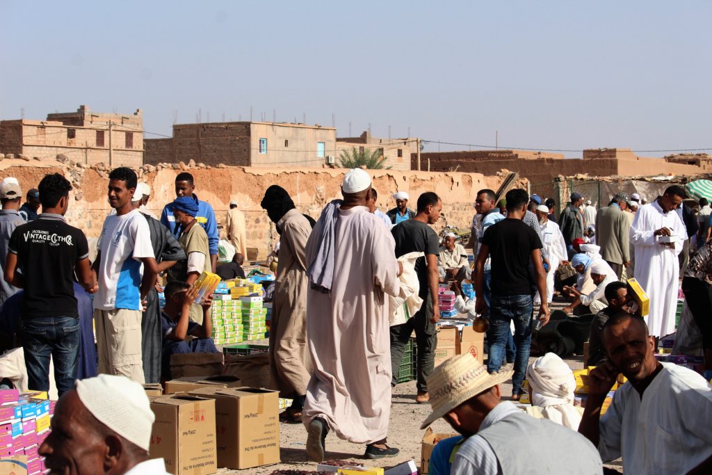 This photo shows lots of people haggling over brightly packaged boxes of dates