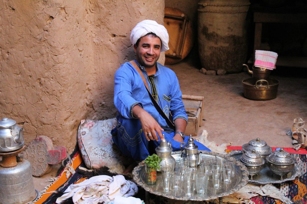 This photo shows Hamid in traditional Berber dress sitting on the floor with a tray of tea glasses in front of him