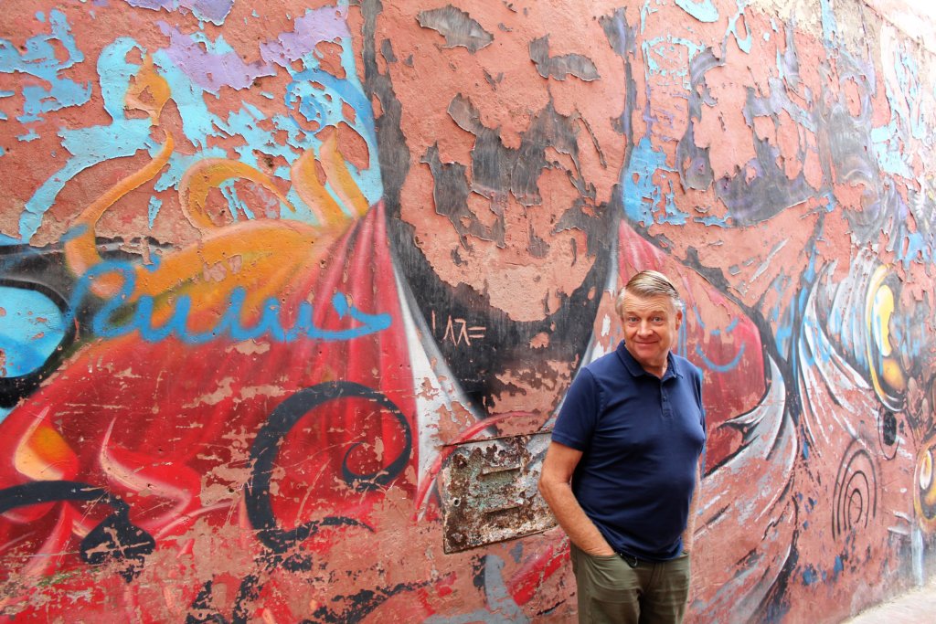 This photo shows Mark standing in front of a peeling wall painting of a man