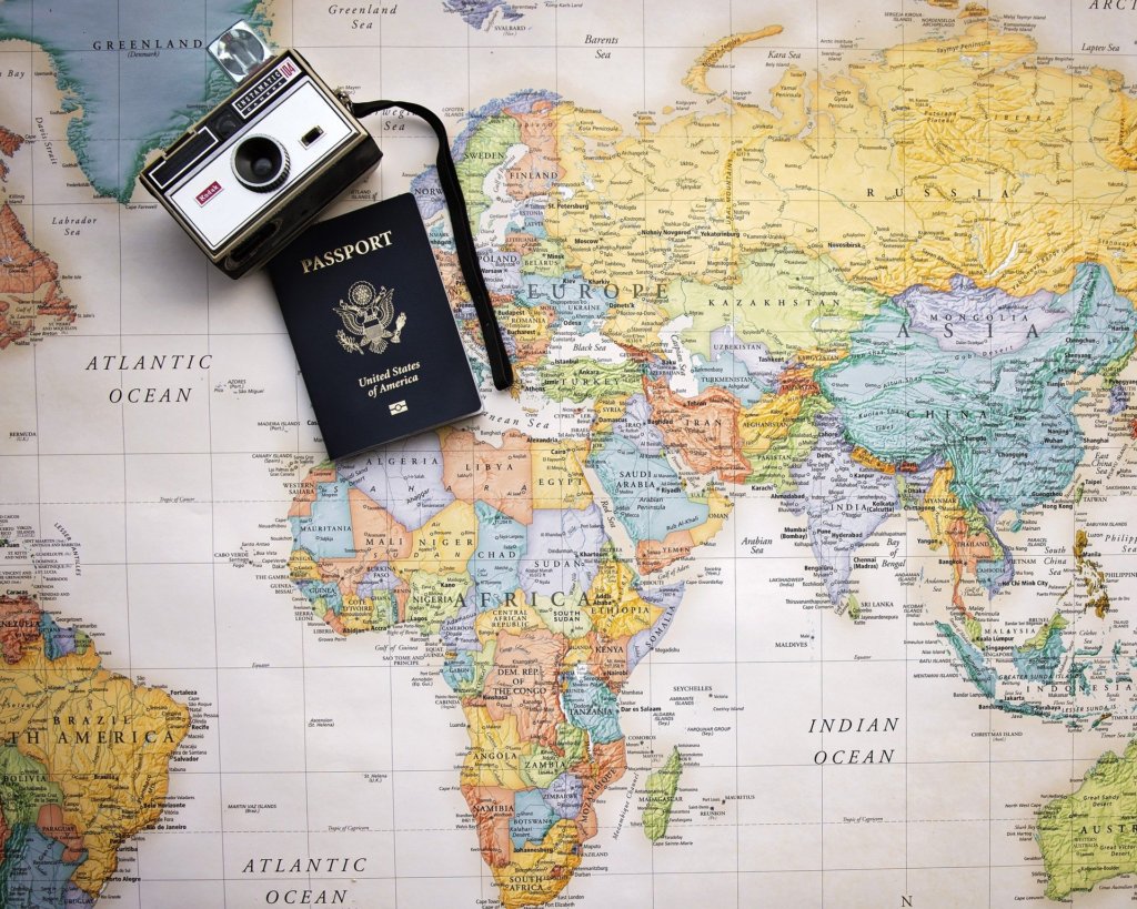 This picture shows a wworld map with a camera and passport on it