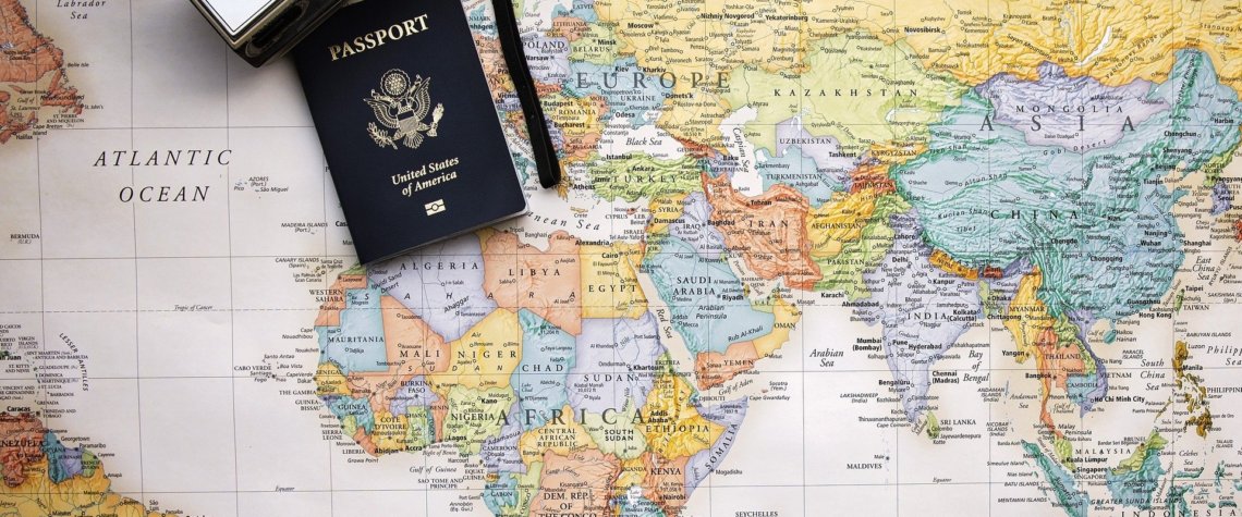 This picture shows a wworld map with a camera and passport on it