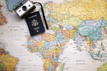 This picture shows a wworld map with a camera and passport on it