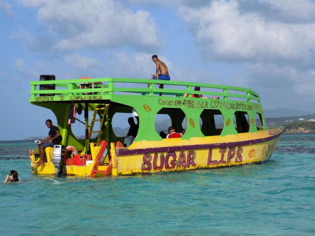 This photo shows a double-decker boat painted emerald green and bright yellow with the name 'Sugar Lips' in red on the side