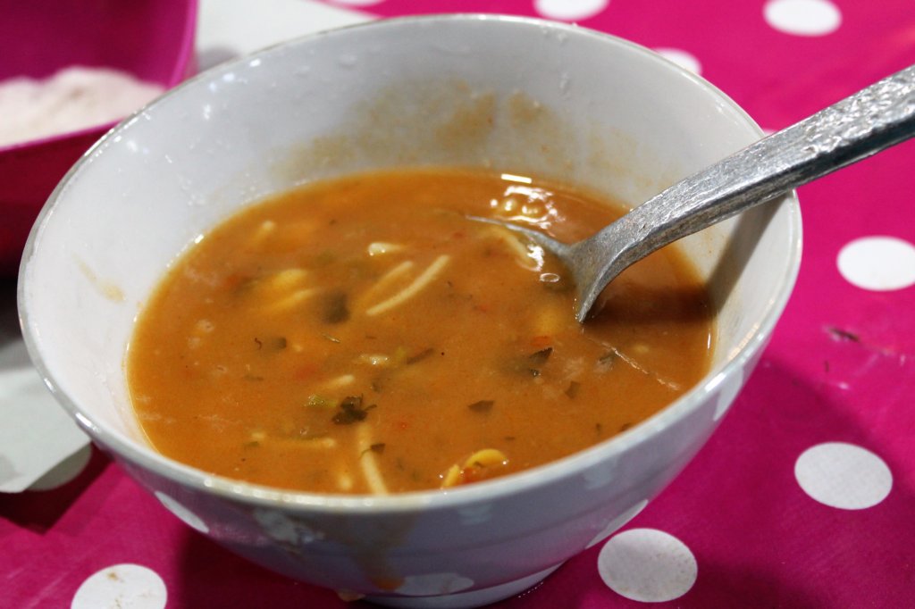 This photo shows a white bowl containing orange-coloured harira soup