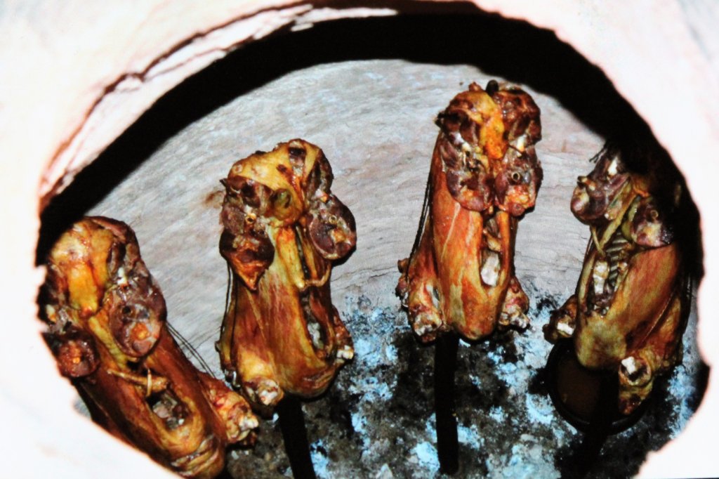 This picture shows four whole lamb carcases roasting in a pit