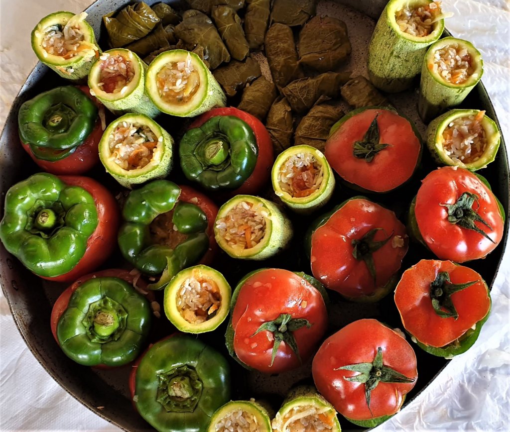 This photo shows a round baking tin filled with stuffed cucumbers, tomatoes and peppers ready for the oven
