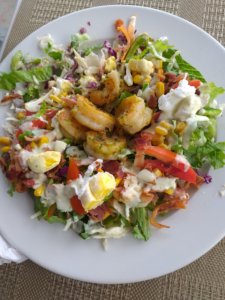 This photo shows a plate of fresh salad topped with prawns and pieces of hard-boiled egg