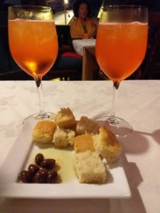 This photo shows two glasses of spritz and a plate of bread and olives