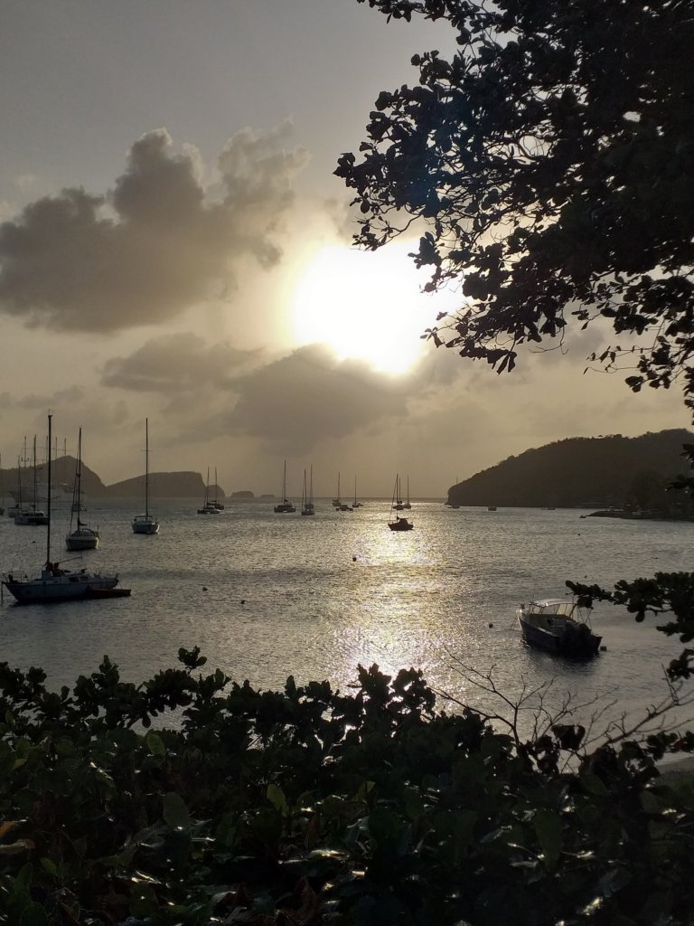 This photo shows moody clouds covering the setting sun behind a bay with yachts in the foreground