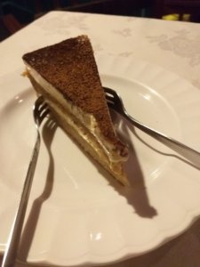 This photo shows a slice of tiramisu on a white plate with two dessert forks