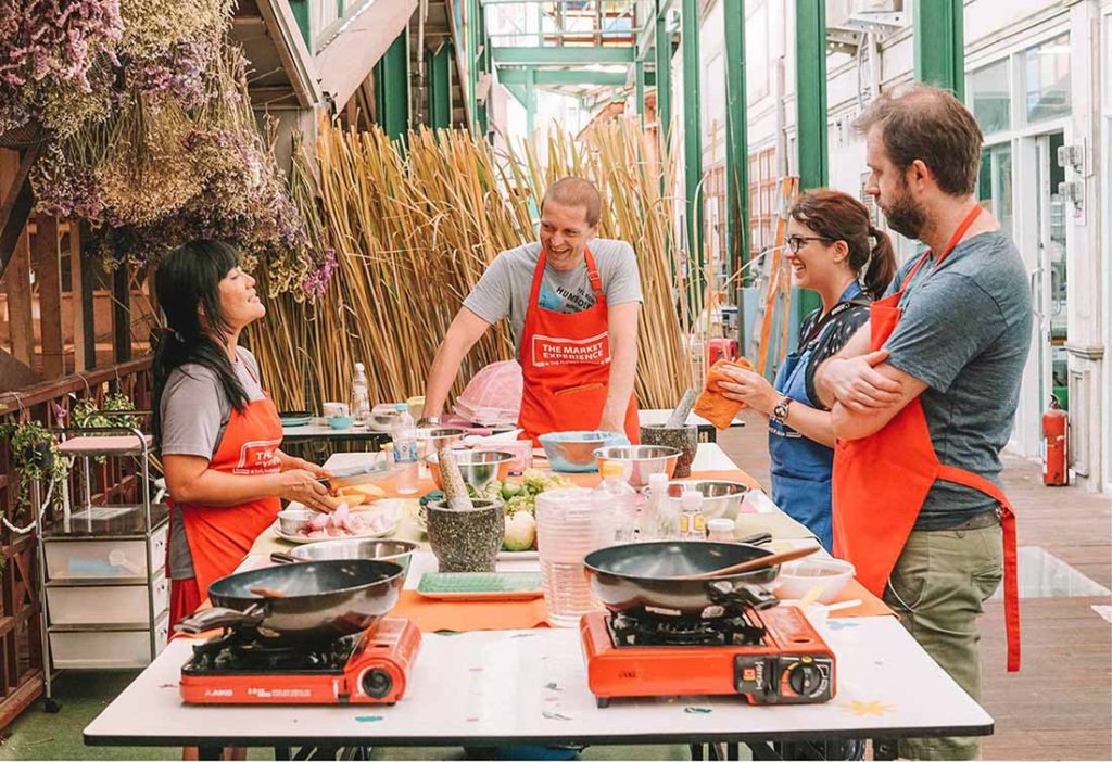 This photo shows students in bright orange aprons learning how to cook Thai food
