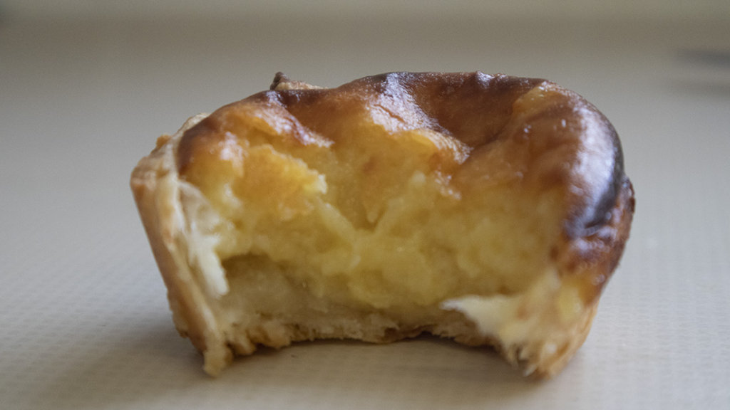 This photo shows an individual Portuguese custard tgart with a bite taken out of it.